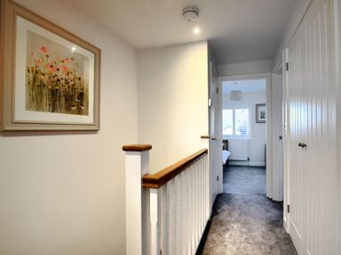 A hallway with carpet flooring a wooden handrail doors and a framed floral painting at Shire View in Lyme Regis