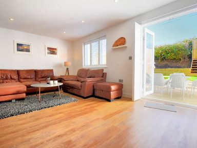 A living room with leather sofas a round coffee table a rug and open doors to an outdoor patio at Shire View in Lyme Regis