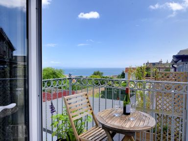 A balcony with a wooden table and chair two wine glasses and a bottle overlooking the sea at Bay View in Lyme Regis