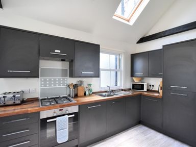A kitchen with dark cabinets wooden countertops a window a skylight a gas stove an oven a toaster a microwave and a sink at Bay View Lyme Regis