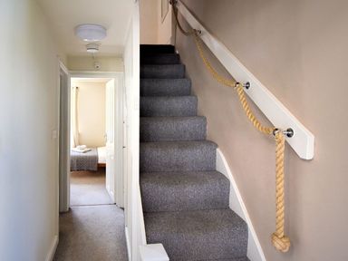 A hallway with carpeted stairs and a rope handrail next to an open door showing a bedroom at Bay View in Lyme Regis