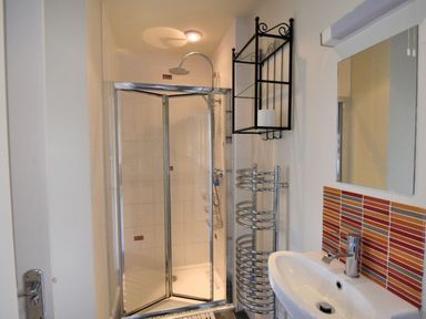 A bathroom with a corner shower, sink, mirror, metal towel rack, and red and orange tiles at Bay View in Lyme Regis