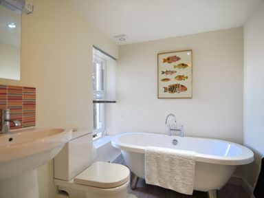 A bathroom with a bathtub towel toilet sink window and a framed fish illustration at Bay View in Lyme Regis