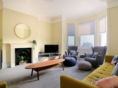 A living room with a yellow sofa two gray armchairs a wooden coffee table a TV on a stand and a fireplace at 7 Seafield Road in Seaton