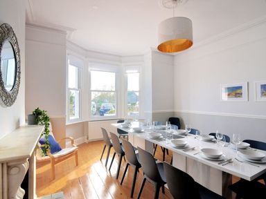 A dining room with a long white table set with dishes and glasses and black chairs around at 7 Seafield Road in Seaton