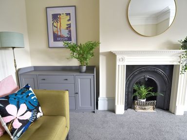 A living room with a fireplace a grey cabinet a yellow armchair and a floor lamp at 7 Seafield Road in Seaton