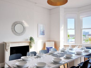 A dining room with a long table set with plates glasses and cutlery next to windows and a fireplace at 7 Seafield Road in Seaton