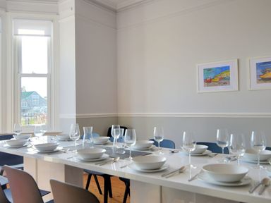 A dining room with a long white table set with white bowls plates cutlery and wine glasses with blue chairs around at 7 Seafield Road Seaton