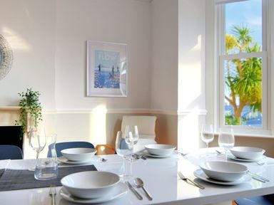 A dining room with a white table set with bowls glasses and cutlery near a window with trees outside at 7 Seafield Road in Seaton