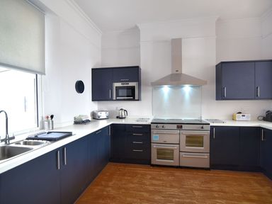 A kitchen with dark blue cabinets a stainless steel oven a microwave and a sink at 7 Seafield Road Seaton