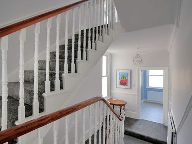 A staircase with grey carpet and white railings next to a hallway with a small table and a framed picture at 7 Seafield Road in Seaton
