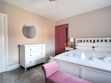 A bedroom with a white bed and dresser a round mirror on the wall and a pink door at 7 Seafield Road in Seaton