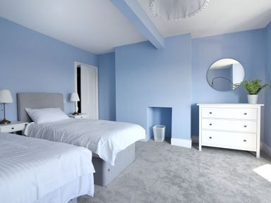 A bedroom with two single beds a white dresser with a round mirror and a plant at 7 Seafield Road in Seaton