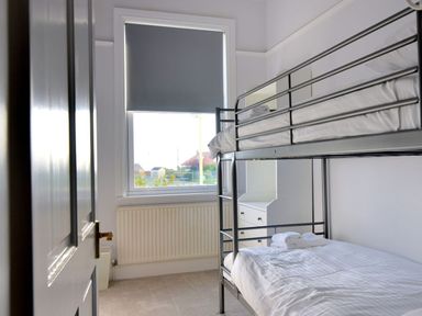 A small bedroom with a metal bunk bed white dresser and a window with a roller blind at 7 Seafield Road in Seaton