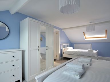 A bedroom with two single beds a white wardrobe with mirrors a white chest of drawers and skylight window at 7 Seafield Road in Seaton