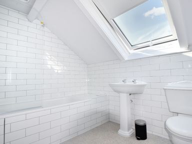 A bathroom with a bathtub a pedestal sink a toilet a small trash bin and a skylight window at 7 Seafield Road in Seaton