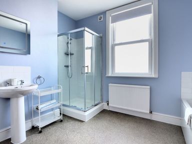 A bathroom with a shower enclosure a pedestal sink a window and a radiator at 7 Seafield Road in Seaton