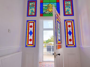 A white doorway with colorful stained glass panels above and beside the door opening to an outdoor area with chairs at 7 Seafield Road in Seaton