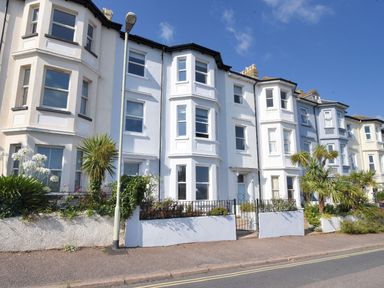 A row of white and light blue townhouses with bay windows and small front gardens with plants at 7 Seafield Road in Seaton