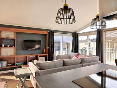 A living room with couches facing a mounted TV and large windows with curtains at Hazelwood 4 Pinewood Retreat in Pinewood