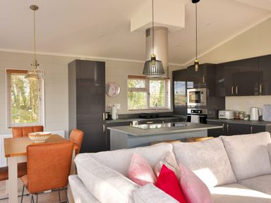 A kitchen and dining area with a wooden table and brown chairs next to a gray sofa with pillows at Hazelwood 4 @ Pinewood Retreat in Pinewood