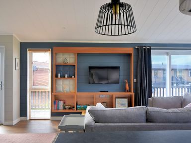 A living room with a mounted TV and wooden shelving unit with books and decor at Hazelwood 4 @ Pinewood Retreat in Pinewood