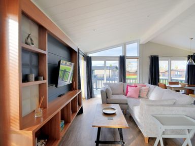 A living room with a wooden entertainment unit a mounted TV a gray sectional sofa with pink pillows and a wooden coffee table at Hazelwood 4 @ Pinewood Retreat in Pinewood