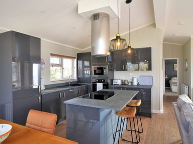 A kitchen with grey cabinets an island with stools and pendant lights at Hazelwood 4 @ Pinewood Retreat in Pinewood