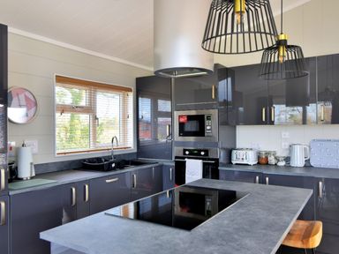 A kitchen with a countertop island stove and cabinets with appliances and a window at Hazelwood 4 @ Pinewood Retreat in Pinewood