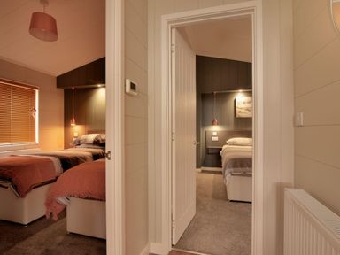 A corridor showing two bedrooms each with a bed bedside light and neutral wall paneling at Hazelwood 4 @ Pinewood Retreat in Pinewood