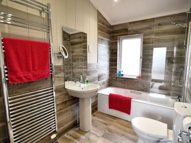 A bathroom with a bathtub shower combination a white sink a toilet and red towels at Hazelwood 4 @ Pinewood Retreat in Pinewood