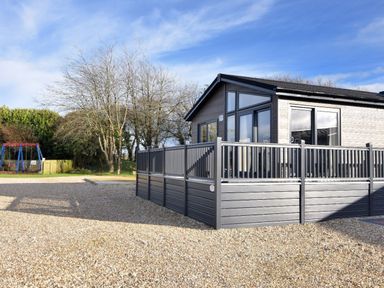 An exterior view of a single-story house with a fenced deck and a swing set in the background at Hazelwood 4 Pinewood Retreat in Pinewood