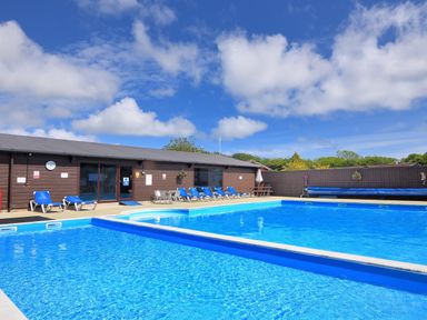 An outdoor swimming pool area with blue lounge chairs and a brown building at Hazelwood 4 at Pinewood Retreat in Pinewood
