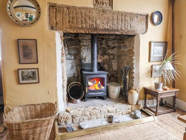 A room with a stone and brick fireplace with a wood stove and basket by the hearth at Old Monmouth in Lyme Regis