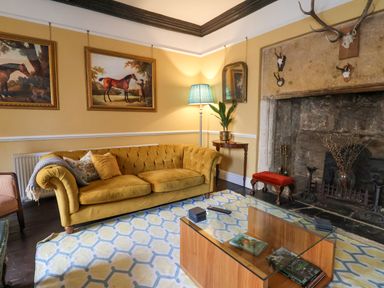 A living room with a yellow sofa paintings of horses on the wall and a stone fireplace at Old Monmouth in Lyme Regis