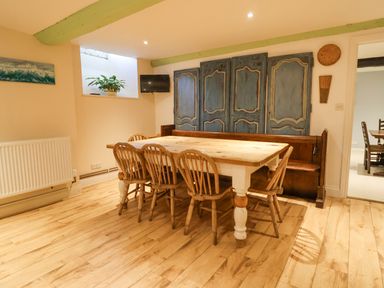 A dining room with a wooden table and chairs blue antique cabinets and a wall-mounted television at Old Monmouth in Lyme Regis