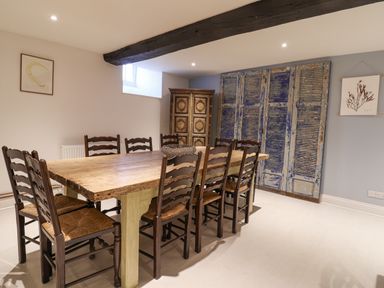 A dining room with a wooden table and eight chairs with a cupboard and blue shutters on the walls at Old Monmouth in Lyme Regis