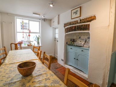 A dining room with a wooden table and chairs a blue cabinet in a fireplace and a window with decorations at Old Monmouth in Lyme Regis