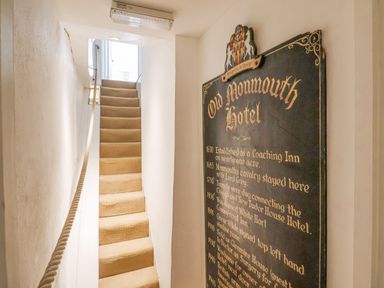 A narrow staircase with carpet and a rope handrail next to a historical sign for Old Monmouth Hotel in Lyme Regis