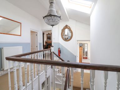A stairway landing with wooden banisters a chandelier a mirror and doorways leading to other rooms at Old Monmouth Lyme Regis