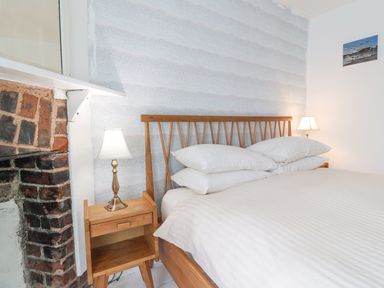 A bedroom with a wooden bed frame white bedding bedside tables with lamps and a brick fireplace at Old Monmouth in Lyme Regis