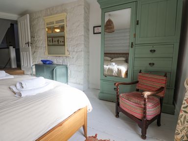 A bedroom with a wooden bed with towels on it a green wardrobe with a mirror a striped armchair and a blue cabinet at Old Monmouth in Lyme Regis