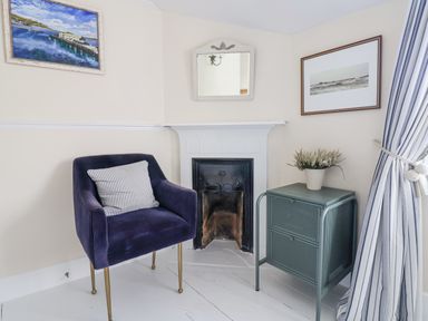 A room corner with a purple armchair with striped cushion a small cabinet with a plant a fireplace two framed pictures and striped curtains at Old Monmouth Lyme Regis