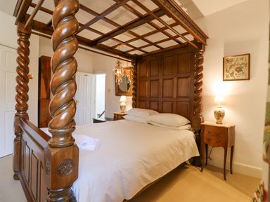 A bedroom with a four-poster wooden bed with white linens bedside tables with lamps and a framed picture on the wall at Old Monmouth in Lyme Regis