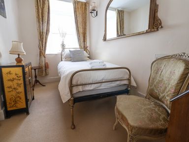 A small bedroom with a single bed a cabinet with a lamp and an upholstered chair at Old Monmouth in Lyme Regis