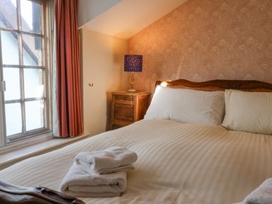 A bedroom with a bed with white striped bedding folded towels on the bed a wooden nightstand with a lamp and a window with red curtains at Old Monmouth in Lyme Regis