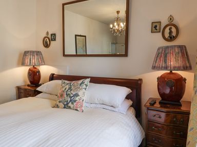 A bedroom with a bed with white linens two bedside tables with lamps and a large mirror above the bed at Old Monmouth in Lyme Regis