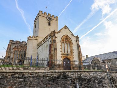 An exterior view of a stone church with a clock tower and arched windows behind a metal fence at Old Monmouth in Lyme Regis