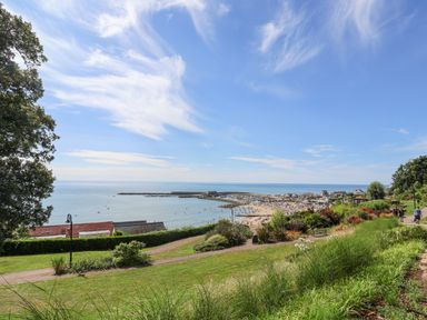 A coastal park with paths, grass, and shrubs overlooking a beach and harbor at Old Monmouth in Lyme Regis