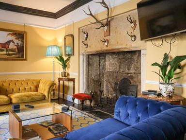 A living room with a blue sofa a yellow sofa a glass coffee table and a fireplace with mounted antlers at Old Monmouth in Lyme Regis